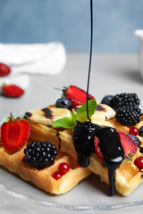 Pouring sauce onto delicious waffles with fresh berries served on grey table