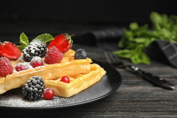 Delicious waffles with fresh berries served on black wooden table, closeup. Space for text