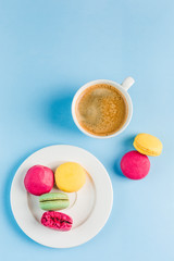 Multicolored macaroons with a white Cup of coffee on a blue background, top view, flat lay with copy space