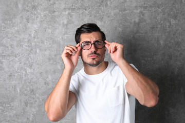 Obraz premium Young man with vision problem wearing glasses on grey background