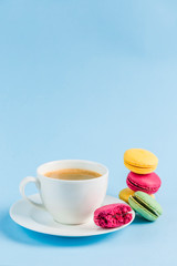 Colorful macaroons with a white Cup of coffee on a blue background, close-up, Flatley with copy space