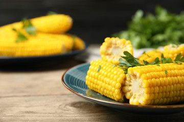 Plate of boiled corn cobs with parsley on wooden table, closeup. Space for text