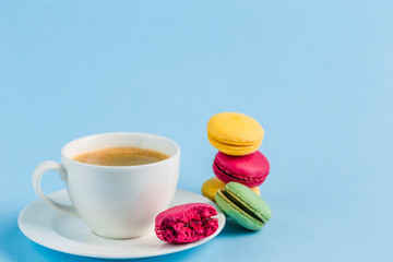 Colorful macaroons with a white Cup of coffee on a blue background, close-up, Flatley with copy space