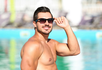 Handsome young man with sunglasses near swimming pool on sunny day