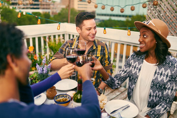 Group of diverse friends having dinner and a glass of wine al fresco in urban setting