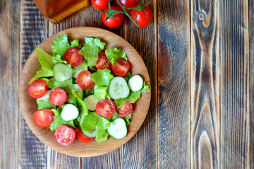 Spring or summer salad with fresh vegetables, cherry tomatoes and cucumbers in a wooden plate on a wooden background Healthy food concept