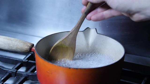 Slow motion - Old vintage pan boiling water on Kitchen hob gas burner, stiring in restaraunt. Wooden Spoon