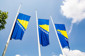 Three bosnian flags in wind on blue sky with clouds
