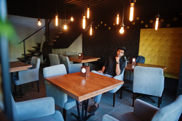 Confident young indian man in black shirt sitting at cafe.