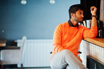 Fototapeta premium Confident young indian man in orange sweater sitting bar counter at cafe.