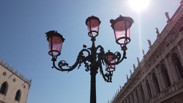 A typical street lamp of Venice (Italy), in the background the sky, the sun and in the corners two buildings.
