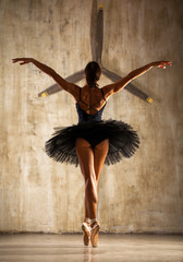 Young beautiful ballerina in black ballet tutu posing in dark studio