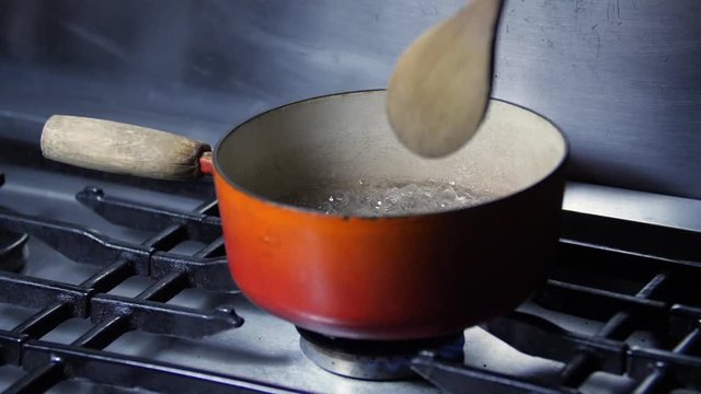 Slow motion - Chef stiring pan of boiling water on stainless steel kitchen cooker hob