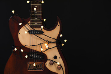 Fototapeta na wymiar Guitar with golden lights on black background, space for text. Christmas music