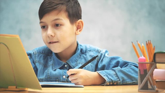 Young concentrated school kid in blue jeans t-shirt writing, copying the text from book on the bookholder.