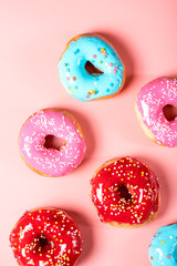 Colorful donuts with icing and topping on a pink background, top view, flat lay. Sweet junk food.