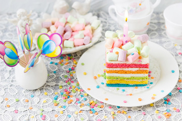 Rainbow birthday cake with marshmallows. Balls,  confetti on the festive table.