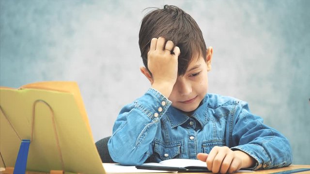 Young clever school kid in blue jeans t-shirt was writing and made a mistake. Now he doesn't know how to correct it.