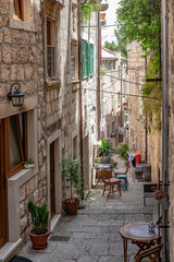 Beautiful narrow old stone street with stone houses and facades, flowers and  and chairs and tables in historic fortified Korcula town, Korcula Island, Dalmatia, Croatia 