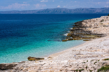 Fototapeta na wymiar Beautiful stone beach on Proizd Island near Korcula Island, Dalmatia, Croatia, blue lagoon, pebbles, clear sea water and blue sky, Croatian islands in background, popular tourist destination 