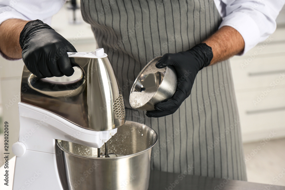 Wall mural Male pastry chef preparing dough in mixer at kitchen table, closeup