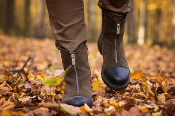 Walking suede leather boots in autumn fallen leaves, front view