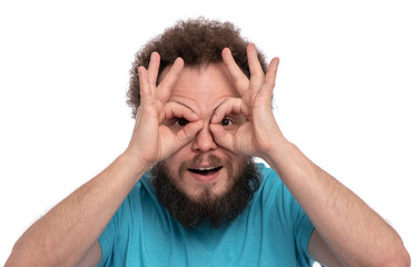 Portrait of handsome bearded man making Ok Gesture with hands on eyes looking through fingers, isolated on white background. Happy crazy smiling caucasian man with funny haircut showing glasses okay.