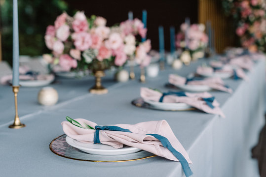Stylish and beautiful wedding table service with blue tablecloth, festive dishes and gentle pink napkins