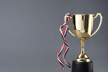 Golden trophy cup with ribbon on grey background. Space for text