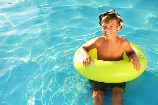 Happy cute boy with inflatable ring in swimming pool