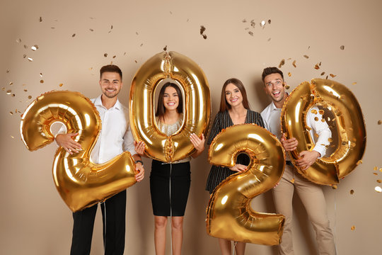Happy young friends with golden 2020 balloons on beige background. New Year celebration
