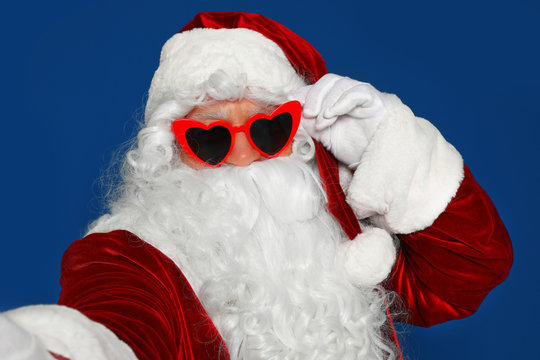 Authentic Santa Claus in sunglasses taking selfie on blue background