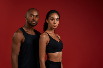 Fototapeta na wymiar Sporty couple. Young african fitness couple in sportswear looking at camera while standing against red background