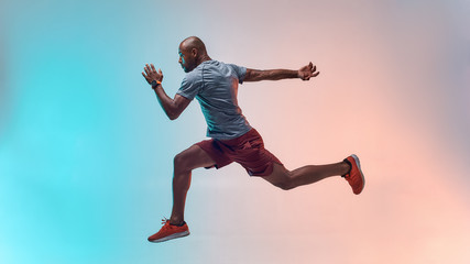 Full length of young african man in sports clothing jumping against colorful background