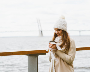 Beautiful young girl drinking coffee, tea from plastic mug in autumn, winter. A woman with long...