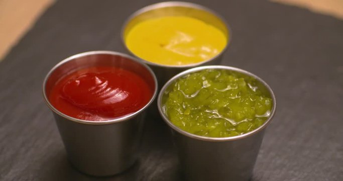 Condiments, ketchup, mustard, and relish displayed on a slate serving board.