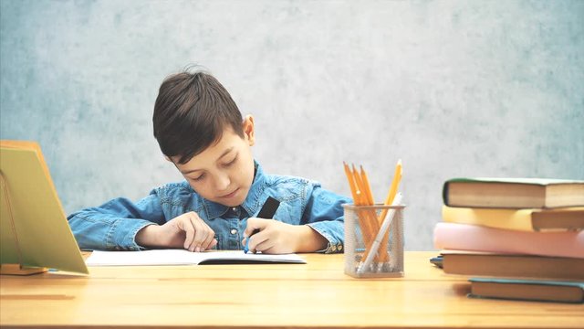 Young concentrated school kid in blue jeans t-shirt writing with a highlighter.
