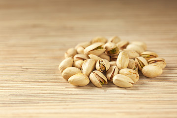 Heap of pistachios on wooden background, close up with copy space