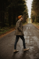 young man in a knitted hat and coat walks along a forest road and smiles