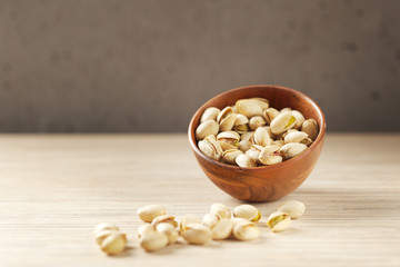 wood bowl of pistachios on wooden background, close up with copy space