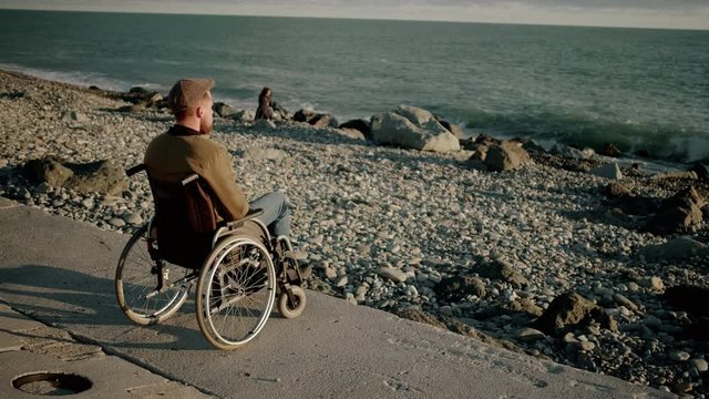 Adult man with paralysis of bottom of body is sitting in sea shore and relaxing