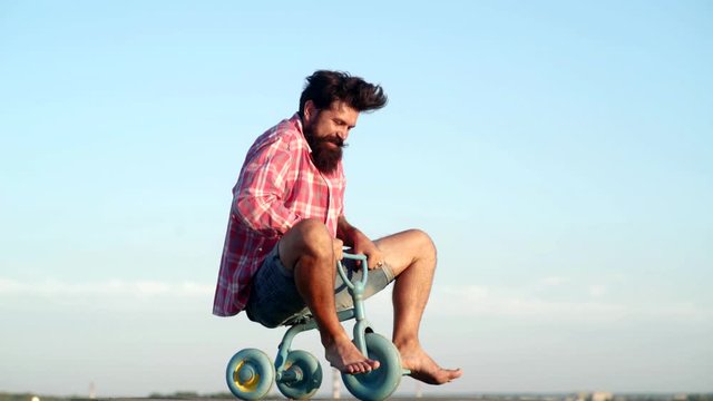 Crazy funny man rides a bike on sky background. Funny man having fun on children bicycle. Hipster with funny face. Different ages. Funny crazy man.