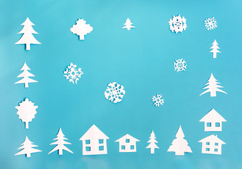 White paper figures of houses, Christmas trees and snowflakes on blue background