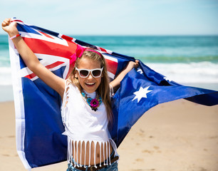 Little girl carries fluttering Australian flag on ocean beach celebrating Australia Day