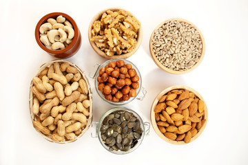Containers filled with different types of nuts and seeds on a white background