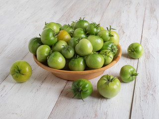 Green unripe tomatoes in a bowl on a white wooden table.