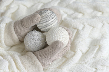 Fototapeta na wymiar Christmas balls in the hands of mittens on a white knitted background. the concept of new year, Christmas , winter