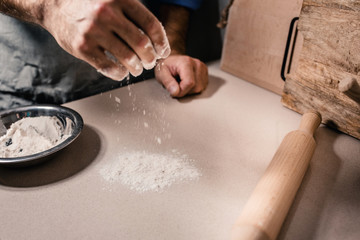 Fototapeta na wymiar In a bakery, a Caucasian baker sprinkles flour on a table preparing a workplace for baking
