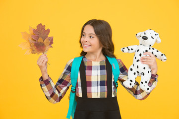 Little schoolgirl with toy backpack and leaves. Happy childhood. Beginning of academic year. Autumn time for studying. Studying in primary school. School education concept. Back to studying