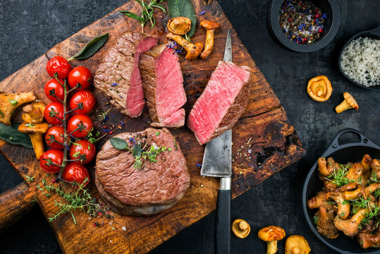 Gebratenes dry aged Rinderfilet Medallion Steak natur mit Tomaten und Pfifferlingen als Draufsicht auf einem Holz Schneidebrett